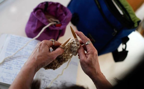The hands of a person knitting using the Yarn Stuff Sack to hold their yarn, also pictured a Maker's Bag.